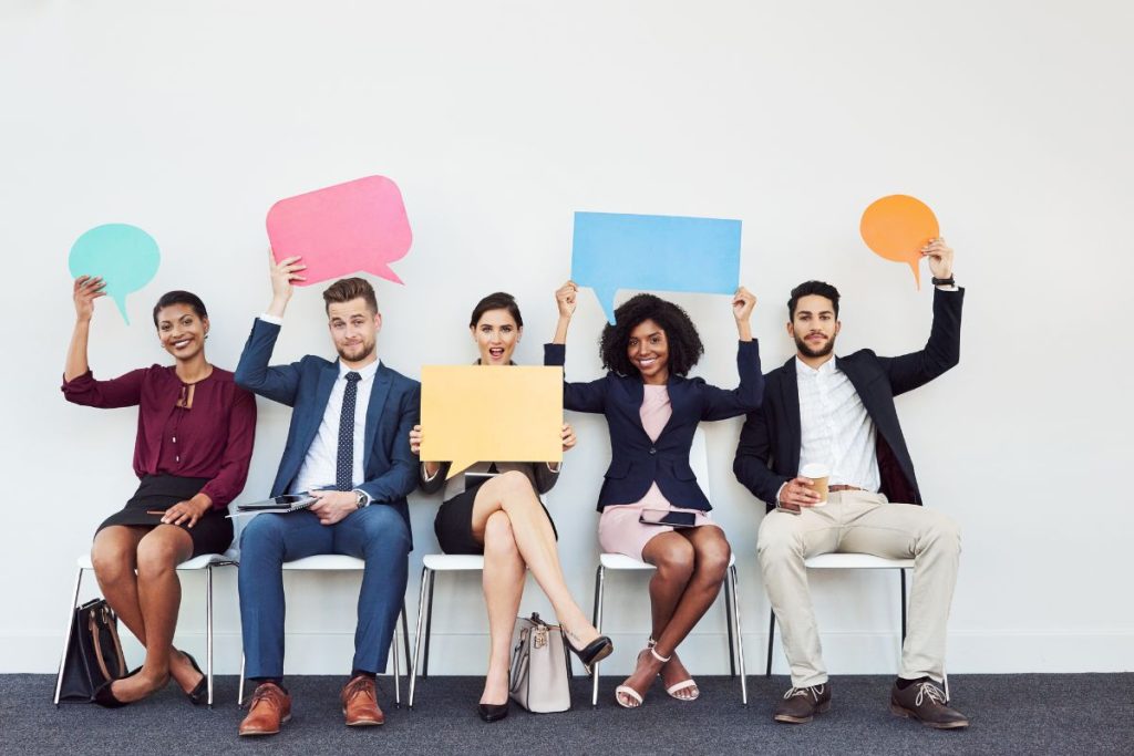 Five professionals sitting in a row holding colorful speech bubble signs.